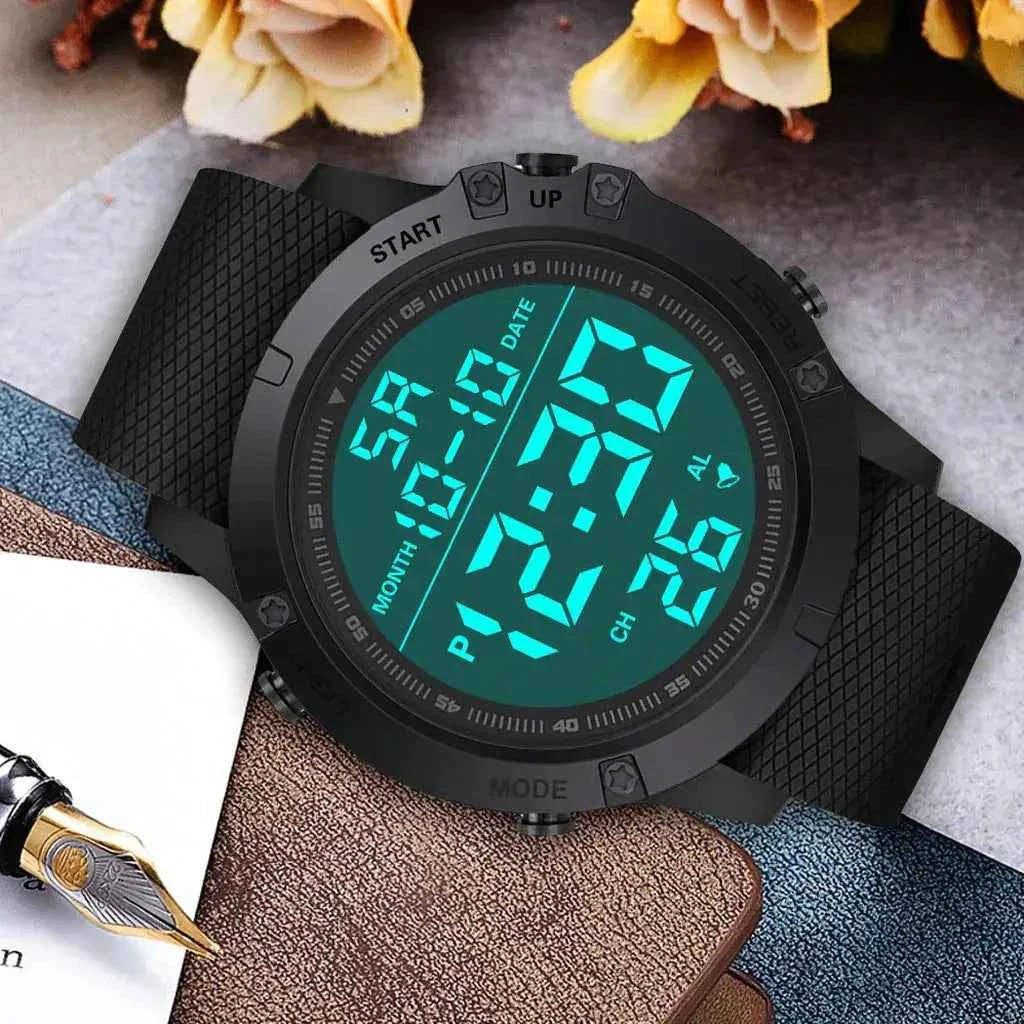 Digital adventure watch with large backlit display on black rubber strap, shown on notebook in lifestyle setting.