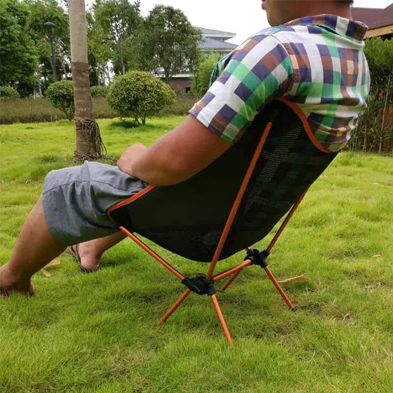 Person relaxing in a lightweight folding camping moon chair with breathable mesh seat and aluminum frame, portable outdoor chair used on grass for camping and backyard lounging